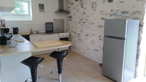 A kitchen with a stone wall, a refrigerator, a stove, a coffee maker, and two bar stools.