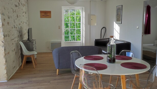 A living room with a dining area, a sofa, a TV, and a window with greenery outside.
