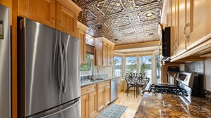 A modern kitchen with stainless steel appliances, wooden cabinets, a granite countertop, and a decorative ceiling.