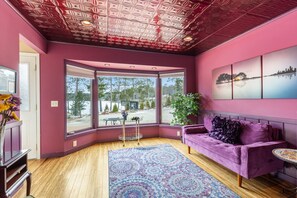 A room with a purple sofa, a patterned rug, and a large window with a view of trees and a building. - 6000 Sq Feet w/Year Around Indoor Pool-King Beds (Crosslake)