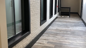 Un pasillo con pared de ladrillo, ventanas amplias, una banca y piso de madera.