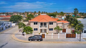 Une maison à deux étages avec un toit recouvert de tuiles rouges, un balcon et une allée où est garée une voiture.