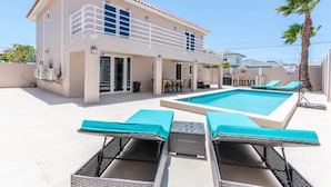 Une maison moderne à deux étages, dotée d’une piscine, d’un espace salon extérieur et d’un palmier.