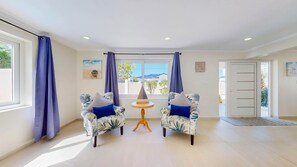 Une pièce comprenant deux fauteuils, une petite table ronde et donnant sur l’extérieur grâce à une fenêtre agrémentée de rideaux.
