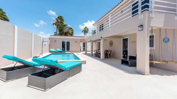 Un espace piscine avec des chaises longues et un coin repas aménagé avec du mobilier d’extérieur.