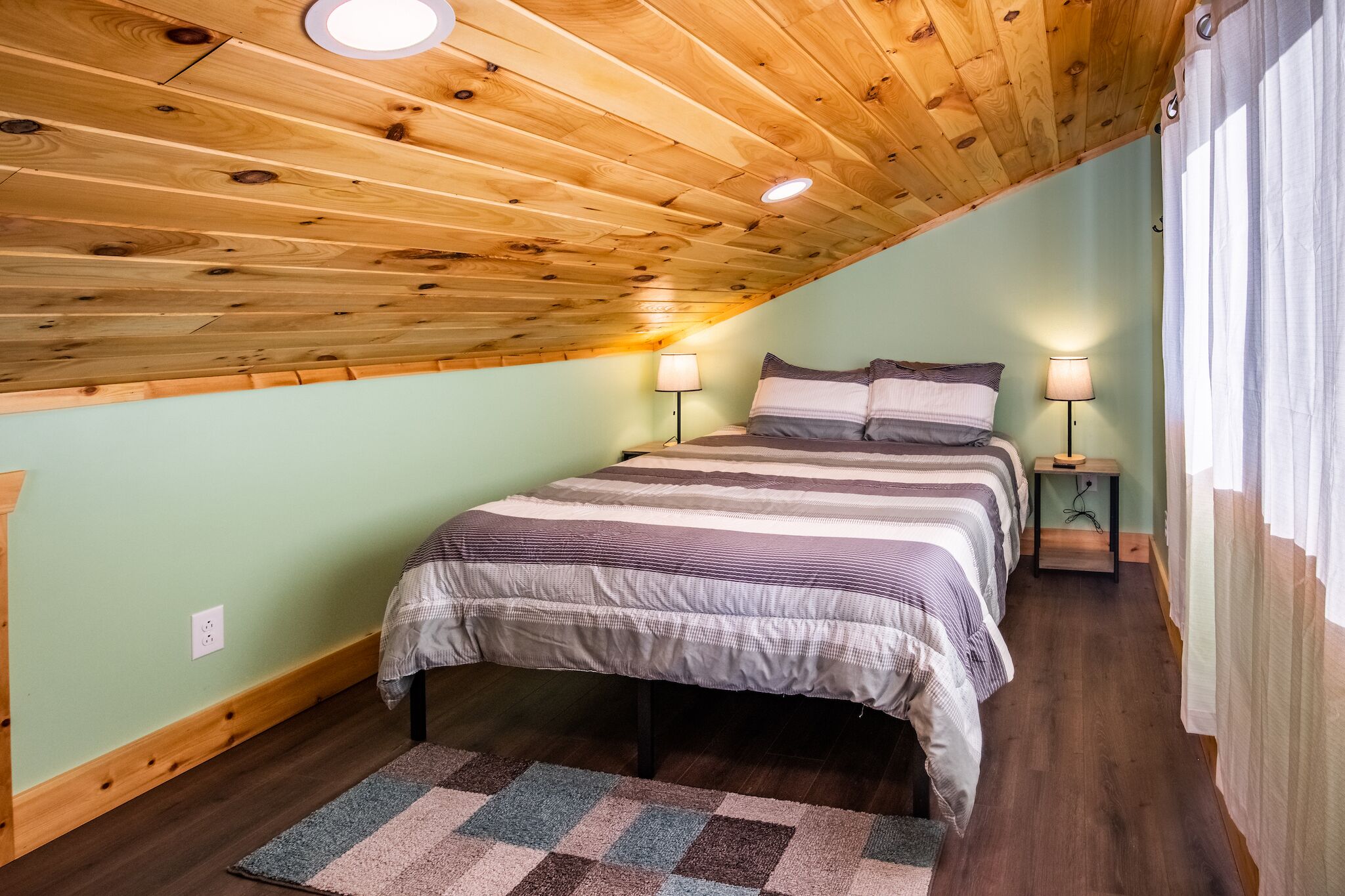 A bedroom with a sloped ceiling, two beds with striped bedding, bedside lamps, and a patterned rug.