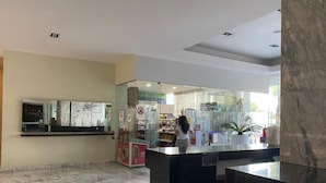 A reception area with a marble floor, a glass partition, and a counter with a person standing behind it.
