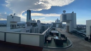 A rooftop terrace with modern architecture, including a cylindrical structure and satellite dishes, offering a panoramic city view.