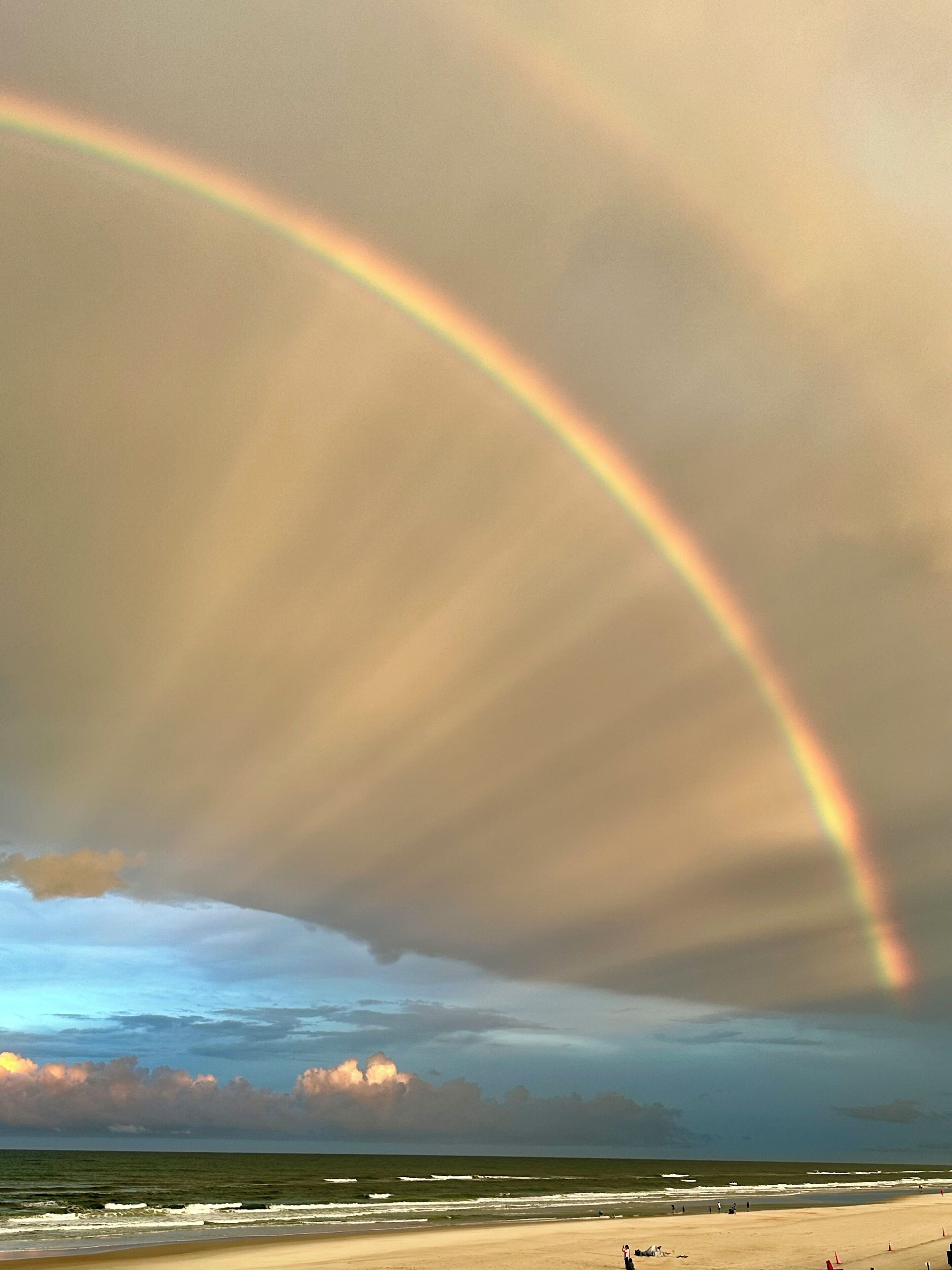 A beach with a rainbow arching over the ocean.