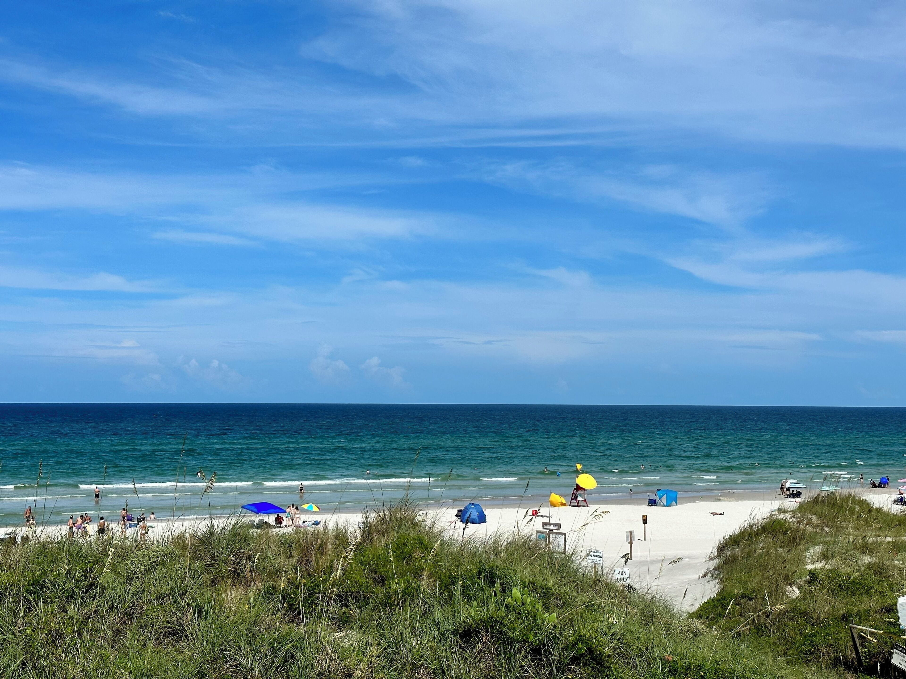 A beach with people, umbrellas, and a clear sky.