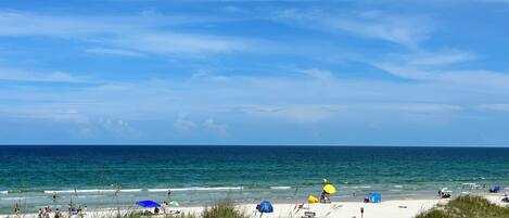 A beach with people, umbrellas, and a clear sky.