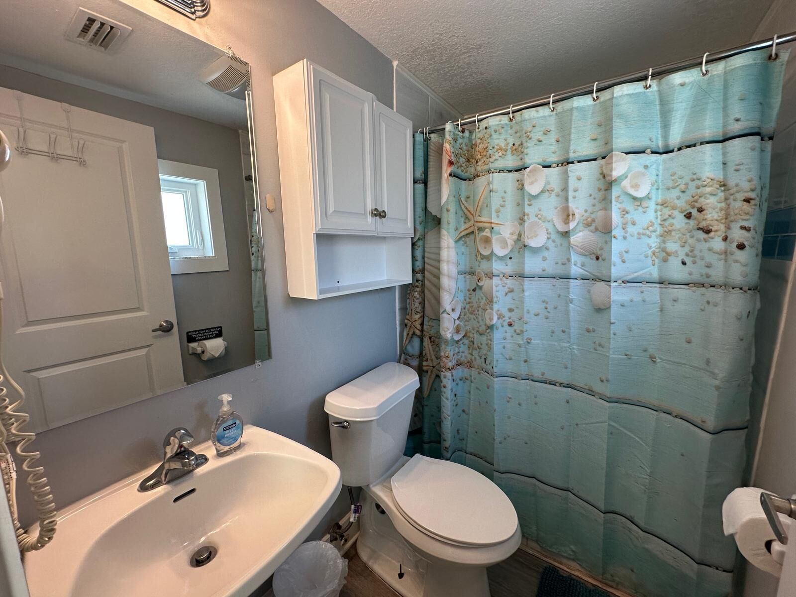Een badkamer met een wit wastafel, toilet en douchegordijn met een schelpenmotief.