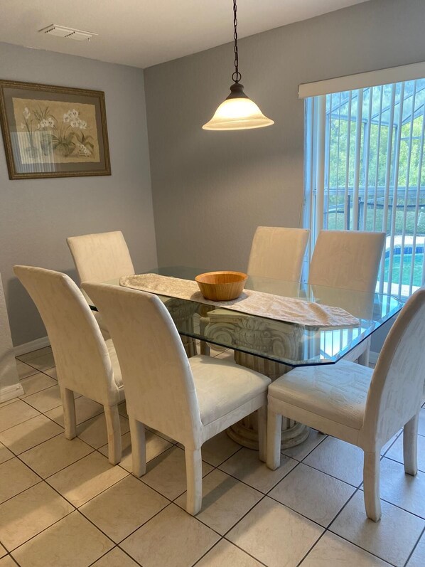 Un comedor con una mesa de vidrio, sillas blancas tapizadas, un cuenco de madera y una lámpara colgante.