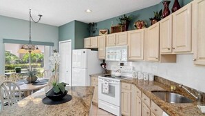 Una cocina con armarios de madera clara, encimera de granito, refrigerador blanco, estufa y fregadero.