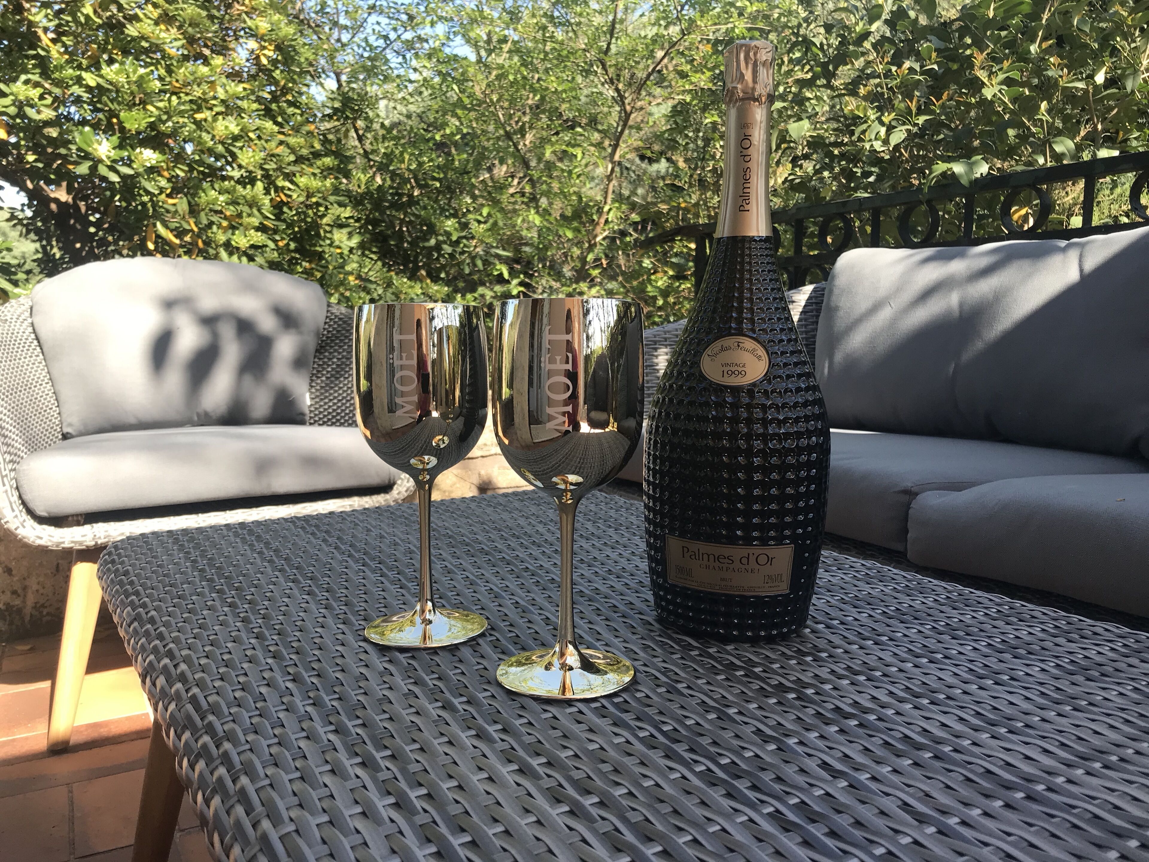 Une bouteille de vin et deux verres sur une table en métal, à l’extérieur.