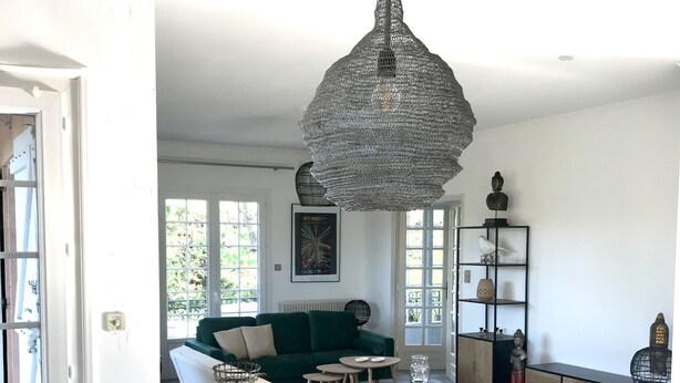Un vaste espace de vie comprenant une table à manger en bois, un canapé vert et un luminaire suspendu.