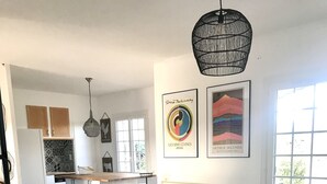 Un salon moderne avec un canapé, une table basse et un canapé d’angle vert. On aperçoit une cuisine à l’arrière-plan, avec une fenêtre et des œuvres d’art accrochées au mur.