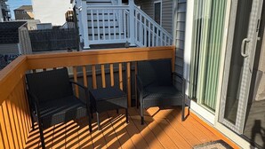 Um deck de madeira com mobiliário externo, guarda-corpo branco e uma porta de correr de vidro.
