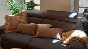 Ein modernes Wohnzimmer mit einem braunen Sofa, zwei Kissen, einem kleinen weißen Tisch und einem Buch mit dem Titel "Kornog".