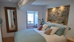 Ein Schlafzimmer mit einem großen Bett, einer Steinwand, Holzboden, einem Spiegel und einem Fenster.