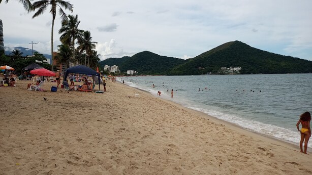 Ein Strand mit badenden Menschen, Palmen und einem Berg im Hintergrund.