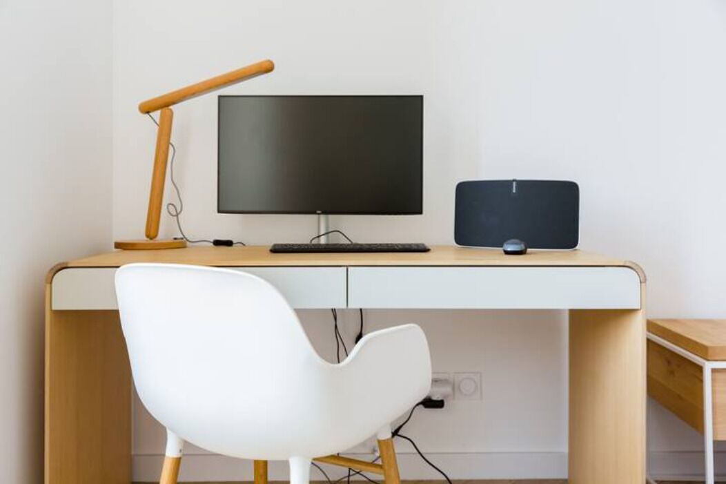 Een moderne werkplek met een bureau, computer, monitor, toetsenbord en een witte stoel.