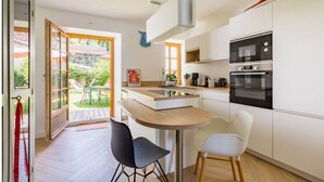 Uma cozinha moderna com armários brancos, forno embutido e um espaço de refeições com duas cadeiras.