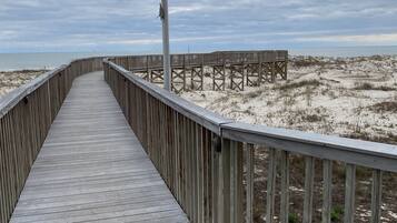 A wooden boardwalk leading to a sandy beach area with a flagpole in the distance.