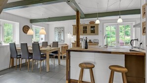 Una cocina con isla de madera, taburetes de bar, una mesa de comedor con sillas y luces colgantes.