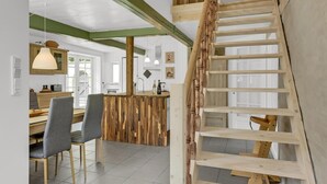 Una cocina moderna con una isla de madera, un comedor con sillas y una escalera de madera.