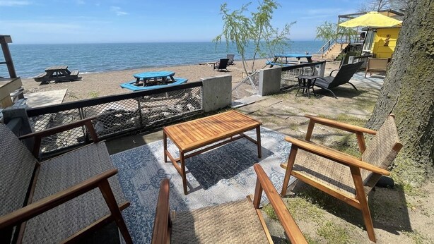 A beachside patio with outdoor seating, a table, and a view of the ocean. - Rustic Beachfront Tiny Cabin Retreat Near Point Pelee (Leamington)