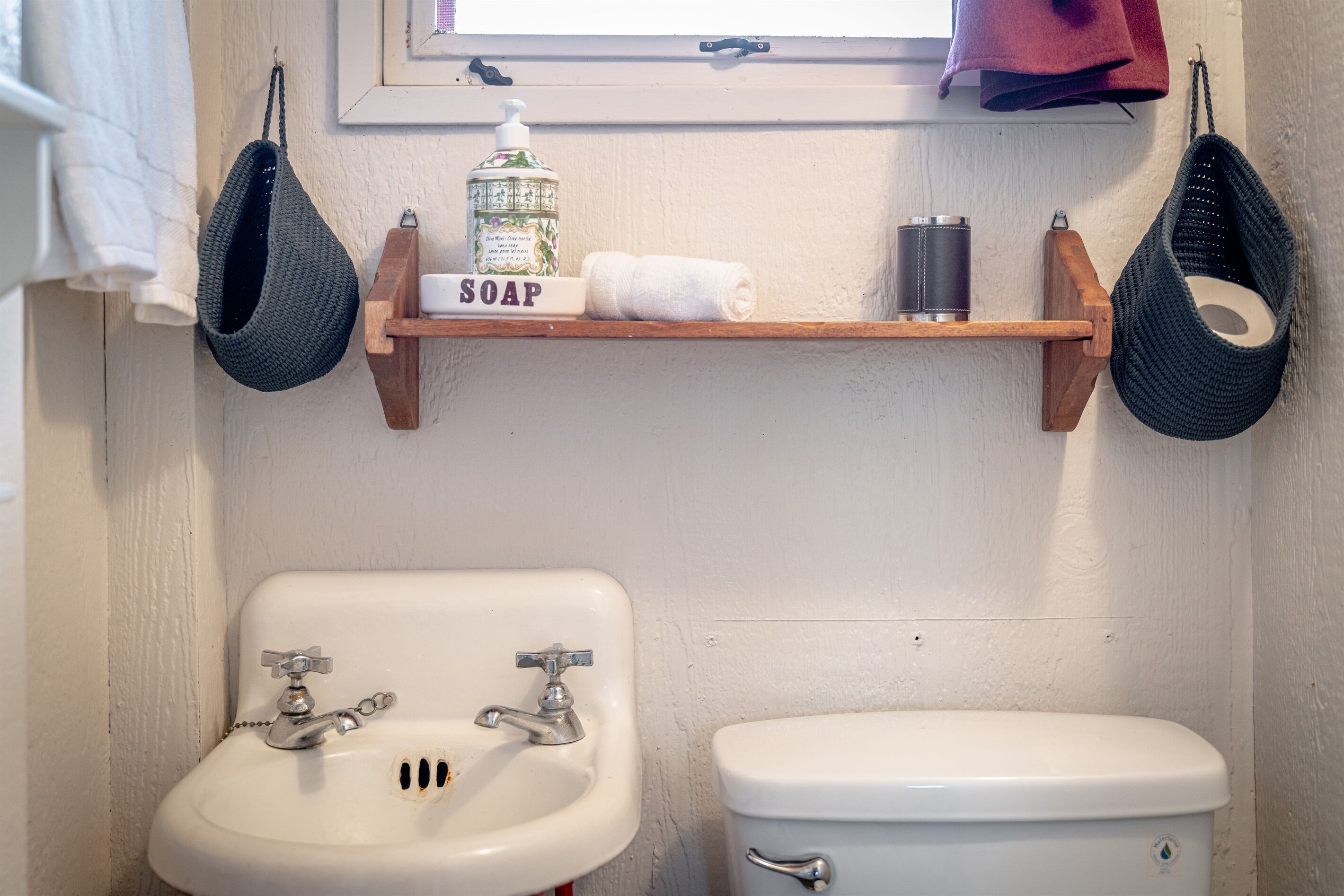 Ein Badezimmer mit einem weißen Waschbecken, einer Toilette und einem Regal mit Seifenspender und Handtüchern.