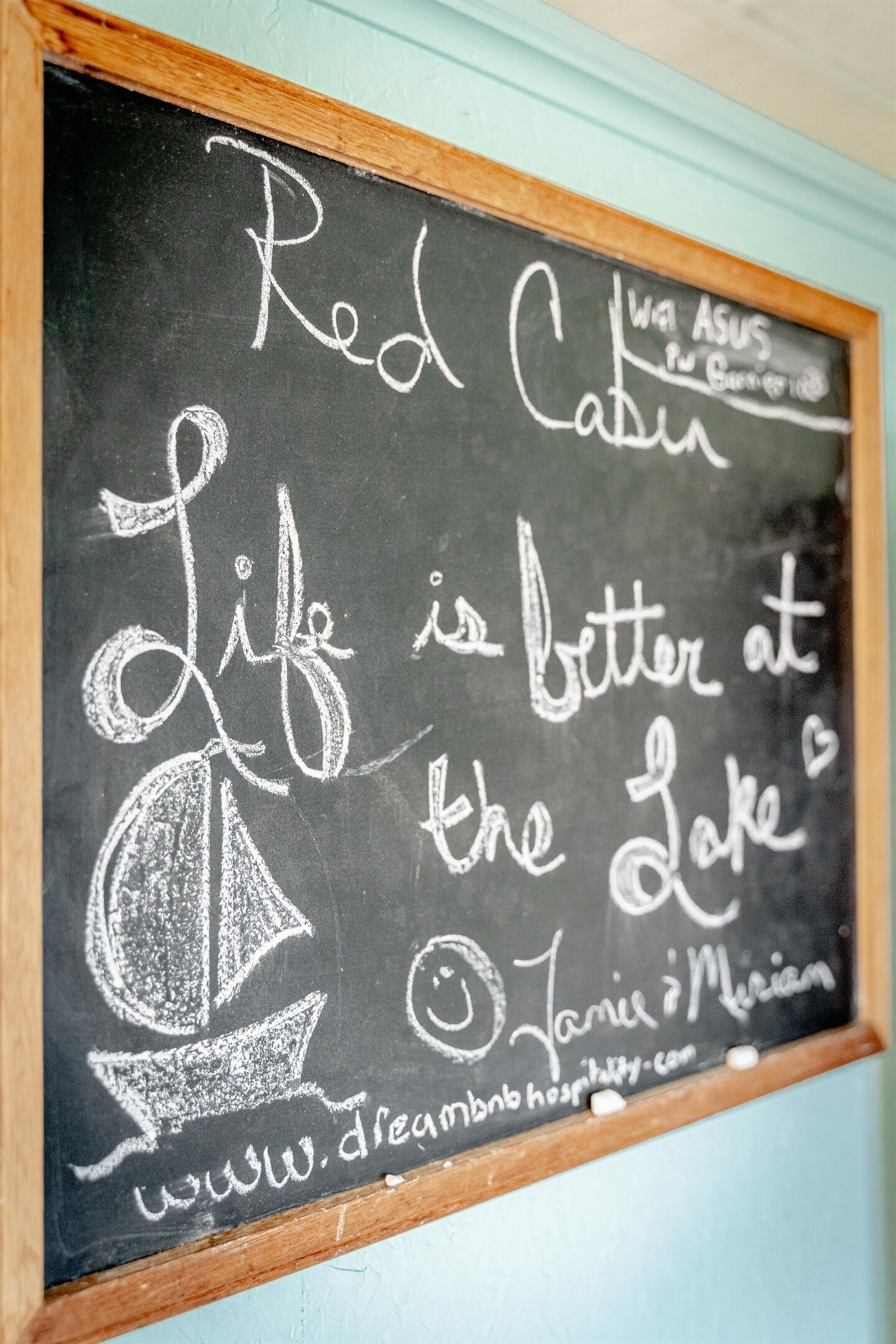Een schoolbord met de tekst 'Red Cabin' en 'Het leven is beter aan het meer', samen met een website-URL.
