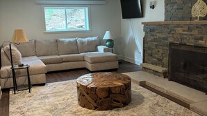 Una sala de estar con un sofá modular, una mesa de centro redonda, una chimenea y un televisor montado en la pared.