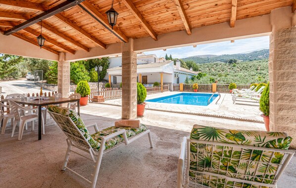 A covered outdoor area with a pool, seating, and a view of a house and landscape.