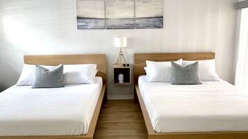 A hotel room with two beds, a ceiling fan, a bedside table with a lamp, and a painting on the wall.