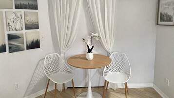 A small room with a round table, two white chairs, a flat-screen TV mounted on the wall, and several framed pictures on the wall.