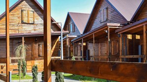 A row of wooden cabins with pitched roofs and large windows, featuring a wooden deck and a small garden area.