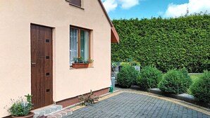 Ein Haus mit gepflasterter Auffahrt, einer Holztür, einem Fenster mit Vorhang und einem Blumentopf.