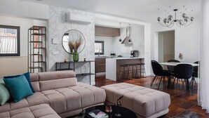 Een moderne woonkamer met een bank, voetenbankje en een salontafel. Er is een eethoek met een tafel en stoelen.
