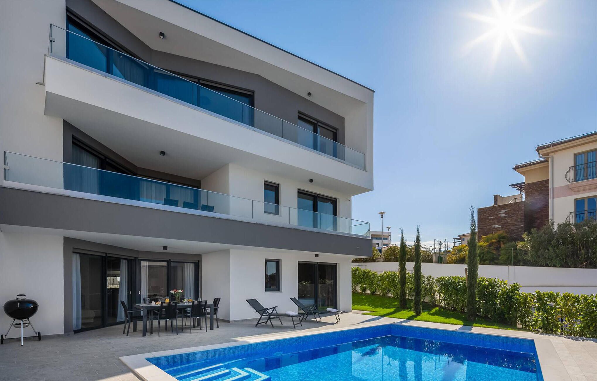 A modern multi-story building with a pool, outdoor seating, and a barbecue area.