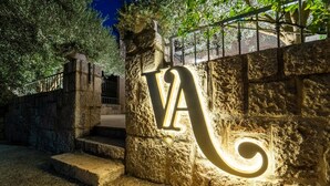 A stone wall with a large illuminated 'A' sign, steps leading up to a gate, and a metal railing above.