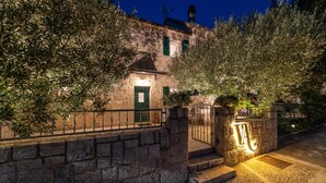 A stone building with a green door, a stone wall, and a gate with a 'V2' sign.