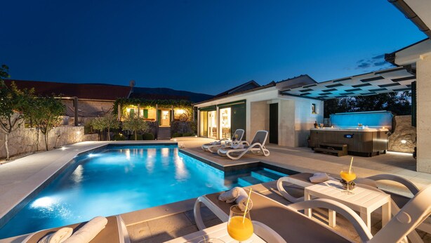 A swimming pool with lounge chairs and a bar area, surrounded by a stone wall and vegetation.
