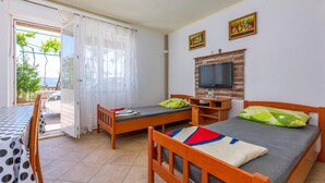 A room with two wooden beds, a TV mounted on a wooden panel, a table with a polka dot tablecloth, and a view of the outdoors through a glass door. - Awesome apartment in Duce with WiFi (Duce)