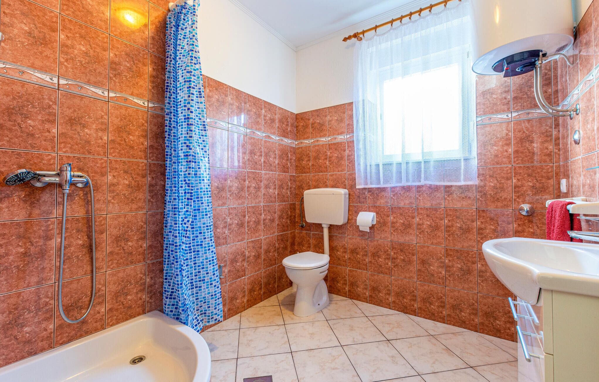 Ein Badezimmer mit Dusche, Toilette, Waschbecken und einem Fenster mit Vorhang.