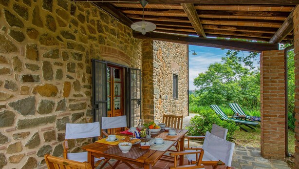 A stone-walled patio with a wooden table and chairs, a view of lush greenery, and a brick wall. - Lovely home in Buggiano with kitchen (Buggiano)