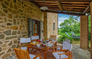 A stone-walled patio with a wooden table and chairs, a view of lush greenery, and a brick wall. - Lovely home in Buggiano with kitchen (Buggiano)