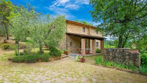 A stone house with a covered porch, surrounded by lush greenery and flowering plants. - Lovely home in Buggiano with kitchen (Buggiano)