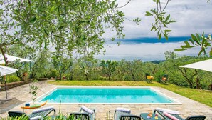 A swimming pool with lounge chairs and umbrellas, surrounded by greenery and a stone pathway. - Lovely home in Buggiano with kitchen (Buggiano)